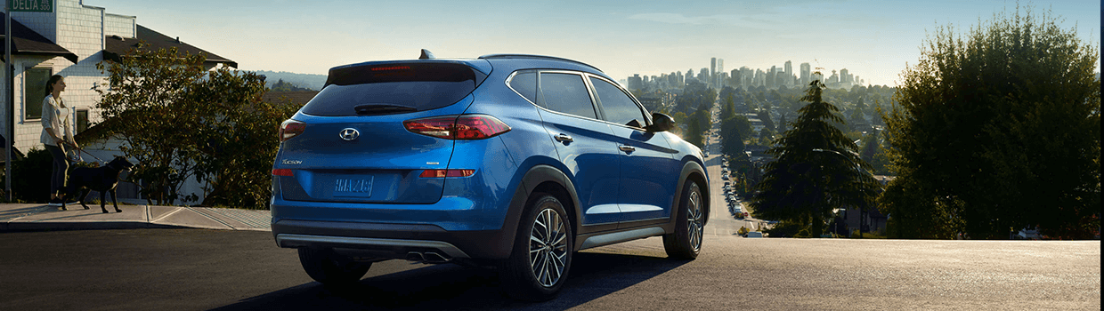 A blue Hyundai SUV turns a corner and looks down a long street to a downtown region