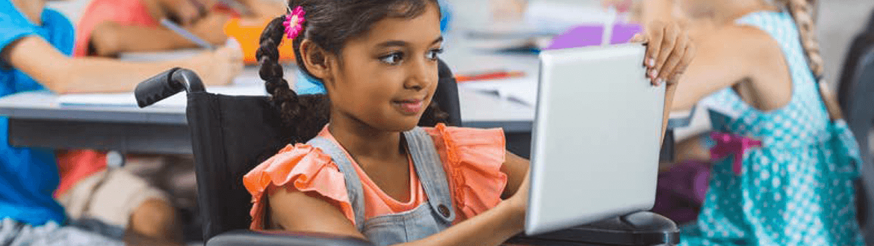 A young girl in a wheelchair smiling as she uses a tablet