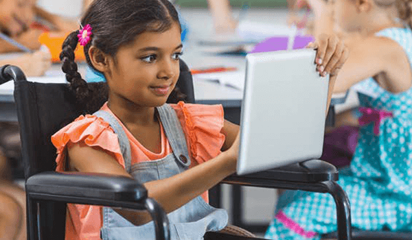A young girl in a wheelchair smiling as she uses a tablet