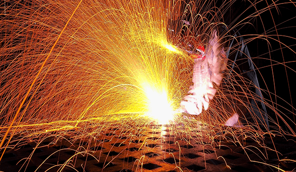 Sparks shooting up from a welder working on a flat metal structure