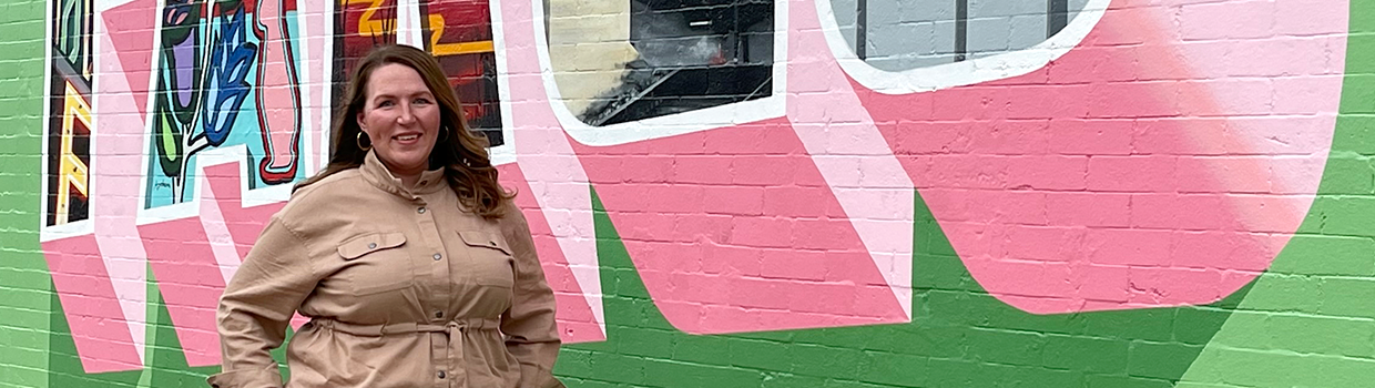 horizontal banner image of Jessica Jarmin standing in front of a Fargo wall mural