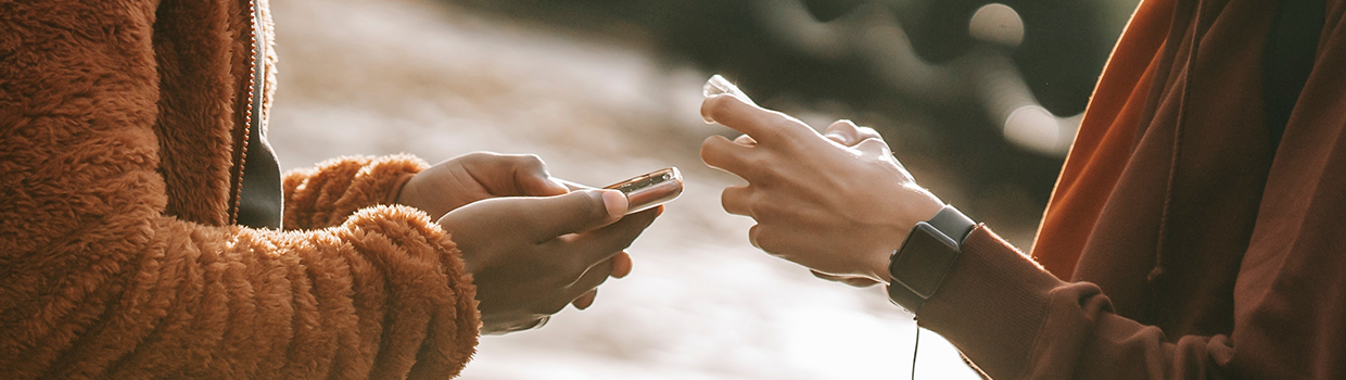 close up of two young adults hands typing on smart phones in front of each other