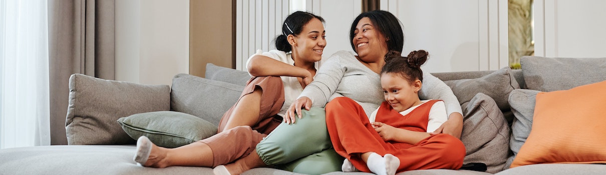 A mother and two daughters sit close to each other and smile on their couch