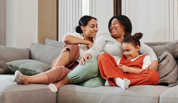 A mother and two daughters sit close to each other and smile on their couch
