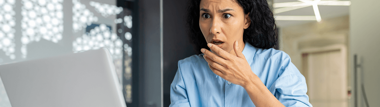 woman at a desk gasping as she looks at her computer screen