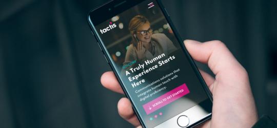 An iPhone being held in a hand showing the Tactis homepage