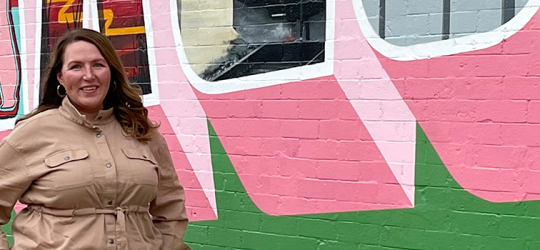 horizontal banner image of Jessica Jarmin standing in front of a Fargo wall mural