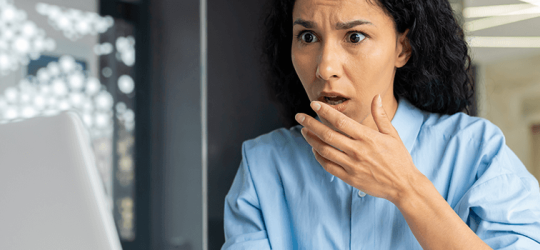 woman at a desk gasping as she looks at her computer screen